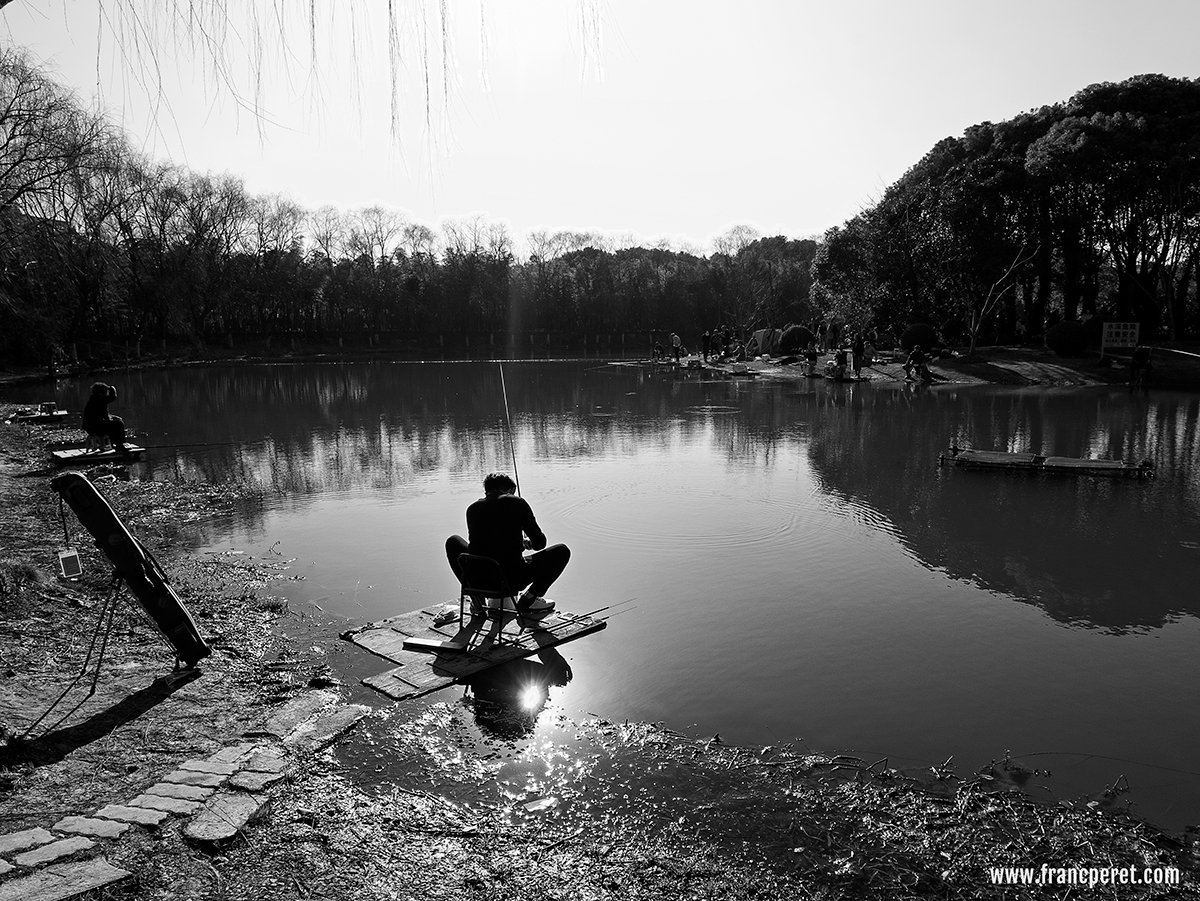 Fisherman in Shanghai Century Park. Path way (dam), lake shape and man posture altogether create motion in the shot even nothing much is happening.